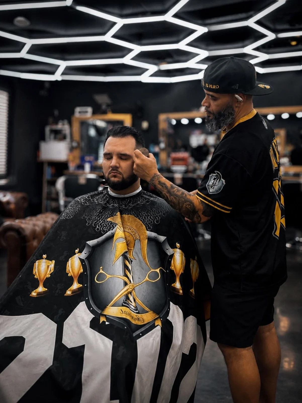 Barber working beside a customer wearing an Imperial Barbershop cape.