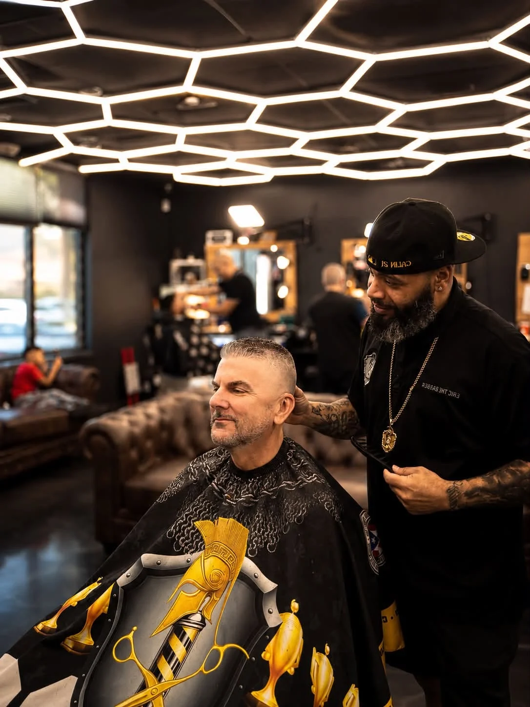 Barber finishing a customer’s short haircut beneath geometric ceiling lights.