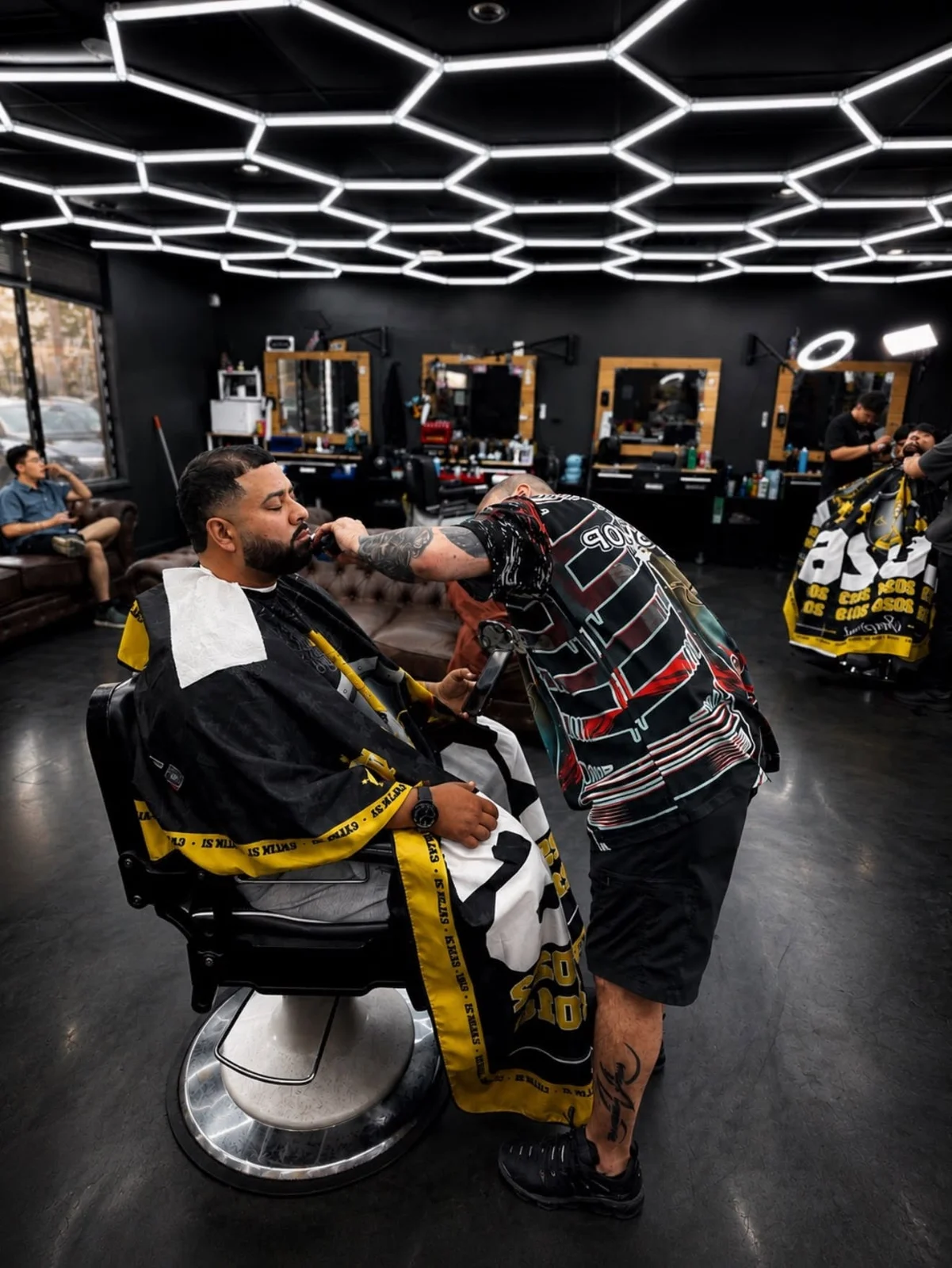 Barber working with a seated customer beneath Imperial Barbershop’s geometric ceiling lights.